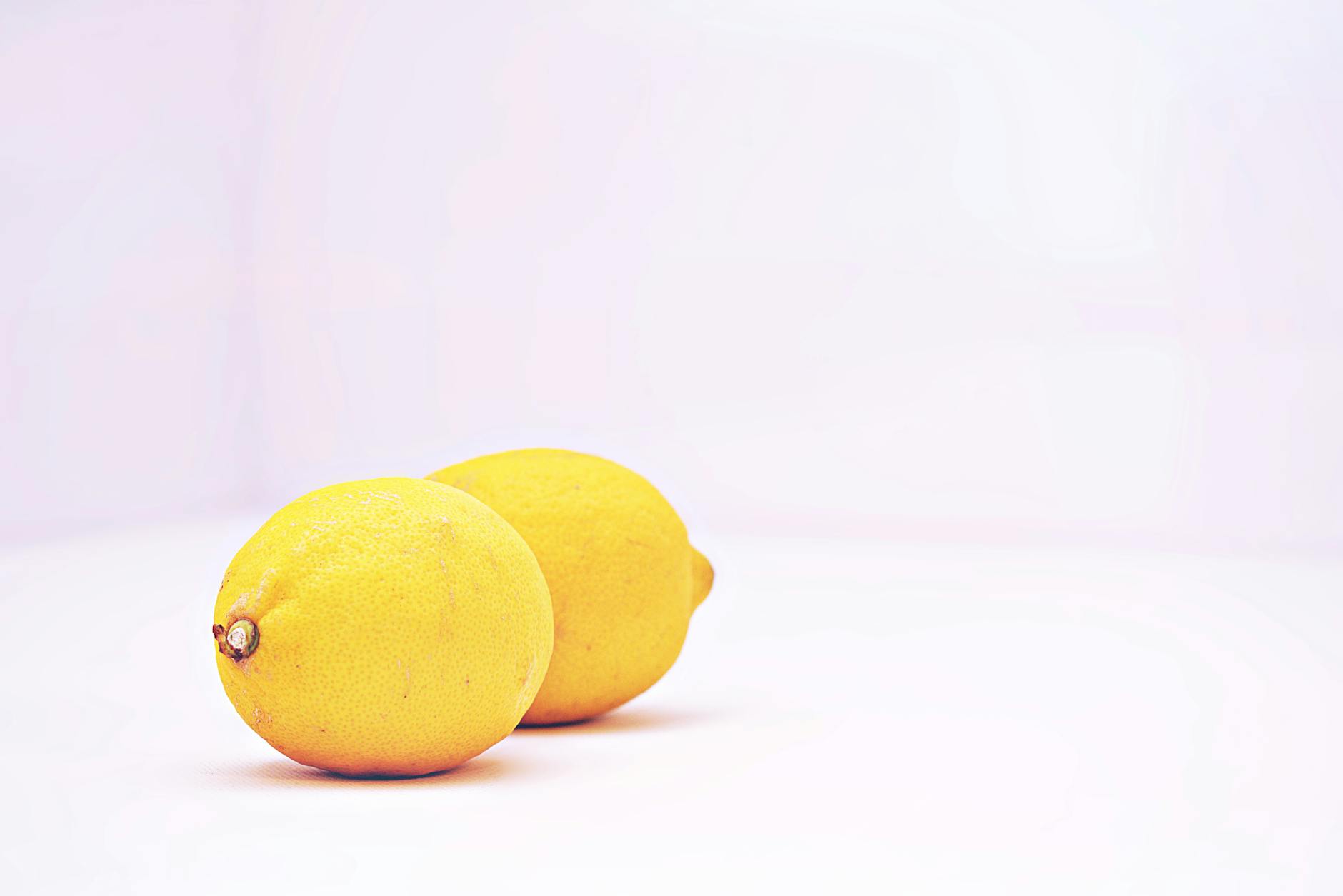 Two vibrant fresh lemons on a minimalist white background, symbolizing simplicity and natural pleasure.