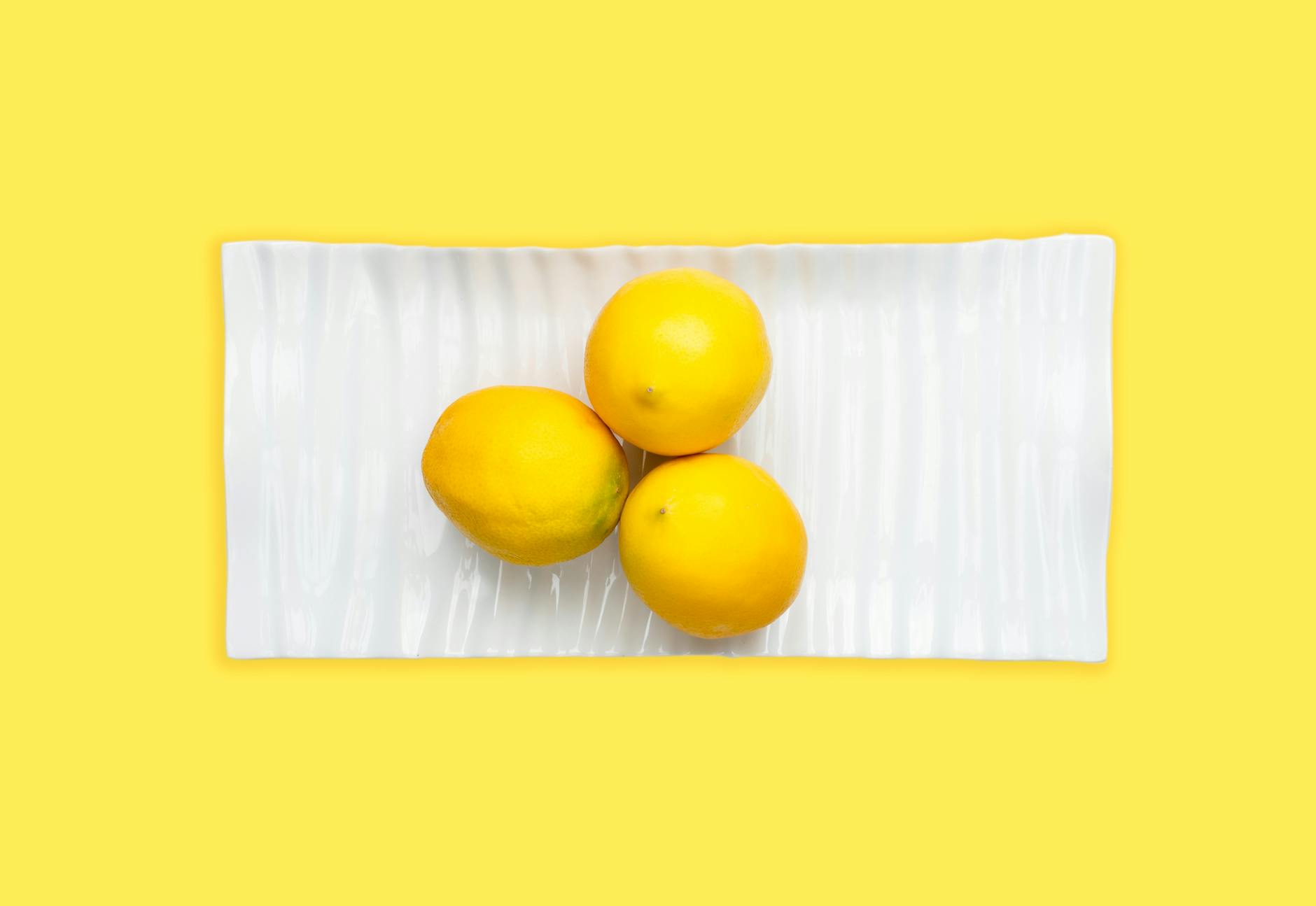 Fresh lemons arranged on a white plate against a yellow background, symbolizing the precision and freshness of targeted clitoral pleasure