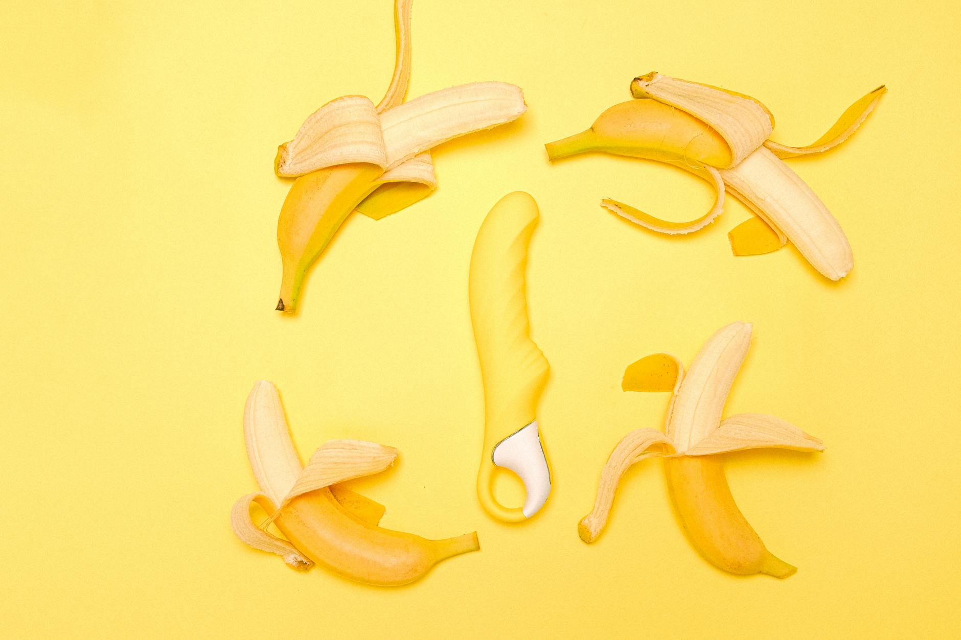 A bright yellow silicone clitoral vibrator arranged with fresh lemons on a yellow background.