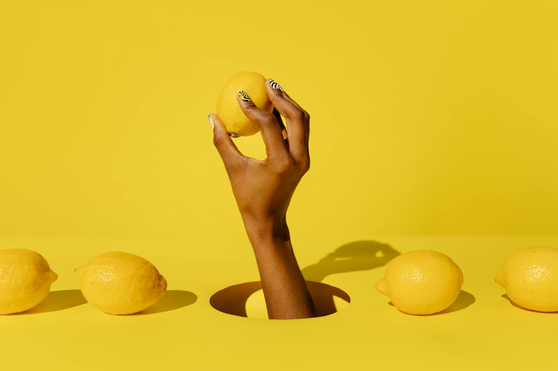 A hand holding a fresh lemon against a vibrant yellow background, symbolizing the bright and refreshing approach to discovering your own pleasure