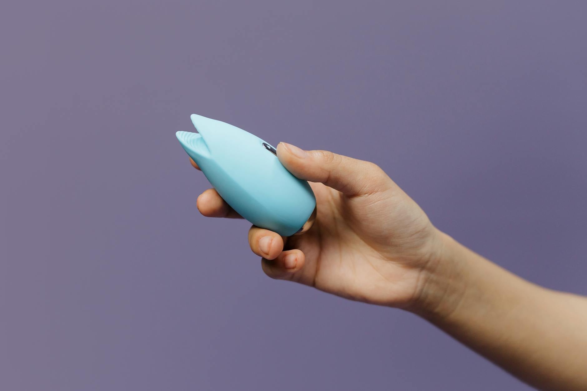 A blue silicone vibrator held gently in hand against a calm purple background, symbolizing self-compassion and reclaiming personal pleasure.